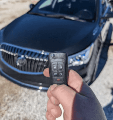 A car locksmith holding a car key fob with a black car in the background.