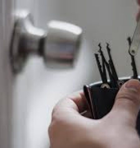 A locksmith holding a set of lock picking tools near a door lock.