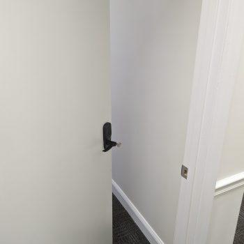 A partially open door with a black handle, revealing a glimpse of a room with a gray carpet.