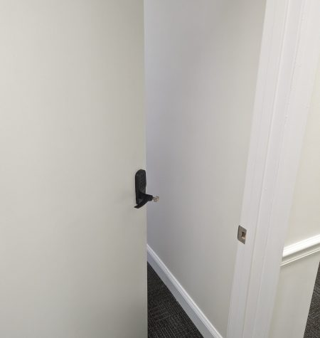 A partially open door with a black handle, revealing a glimpse of a room with a gray carpet.