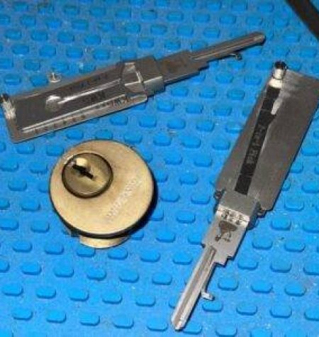 Lock cylinder and two disassembled lockpick tools on a blue textured surface, highlighting the precision work of an emergency locksmith.